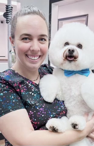Krysti Lee holding a freshly groomed bichon with a blue bow